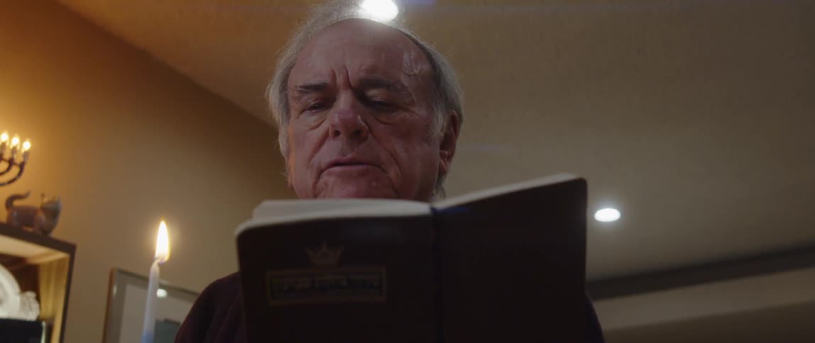 Elderly person holding a candle and reading a bible while standing