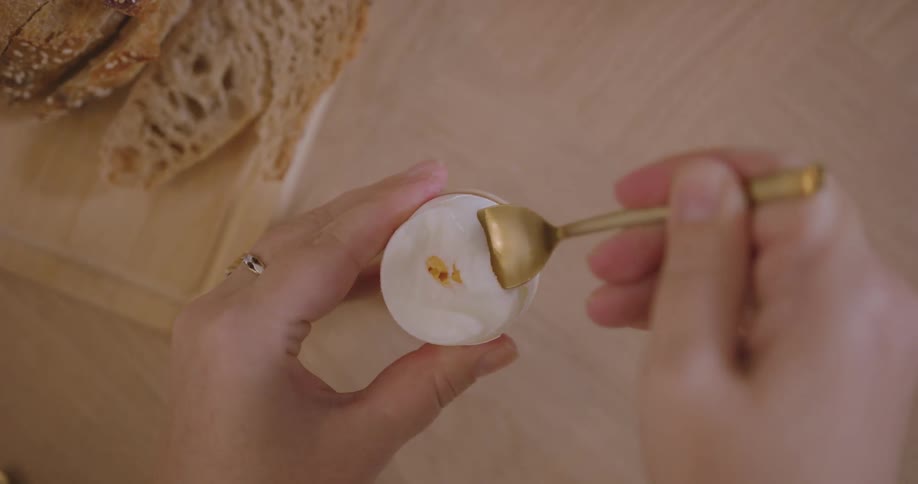 Woman spoons up boiled egg using a spoon
