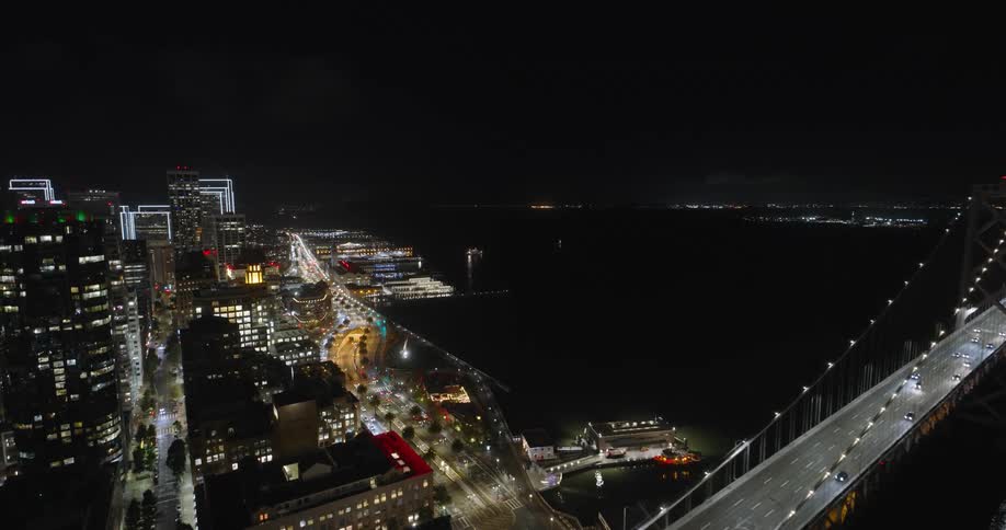 Traffic crosses brightly lit bridge over water at night near downtown