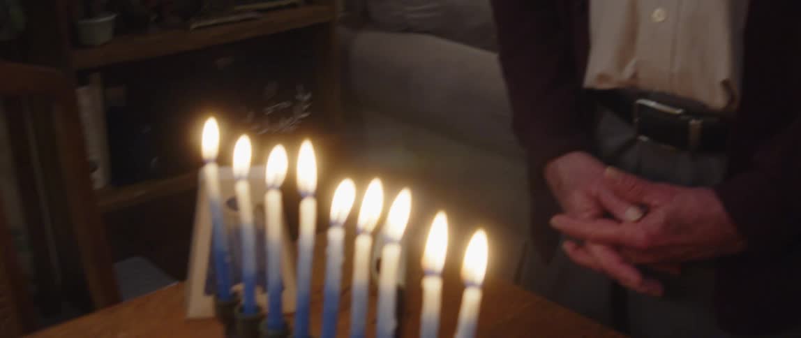 Jewish man praying in front of a menorah at home