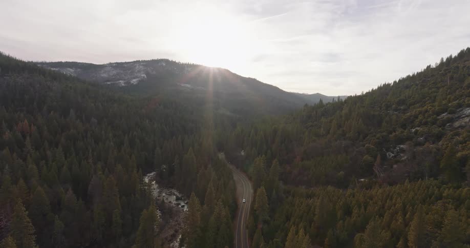 Aerial of highway between forest and mountains during sunset