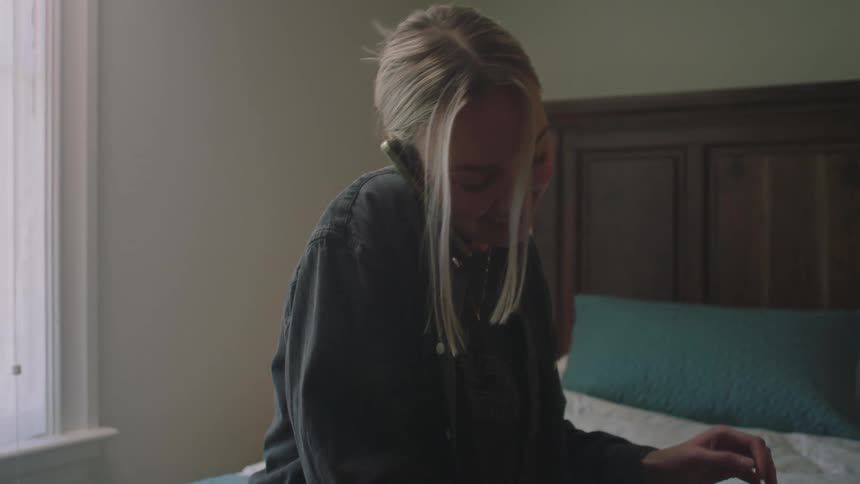 Blonde woman wearing a shirt talks on smartphone on the bed