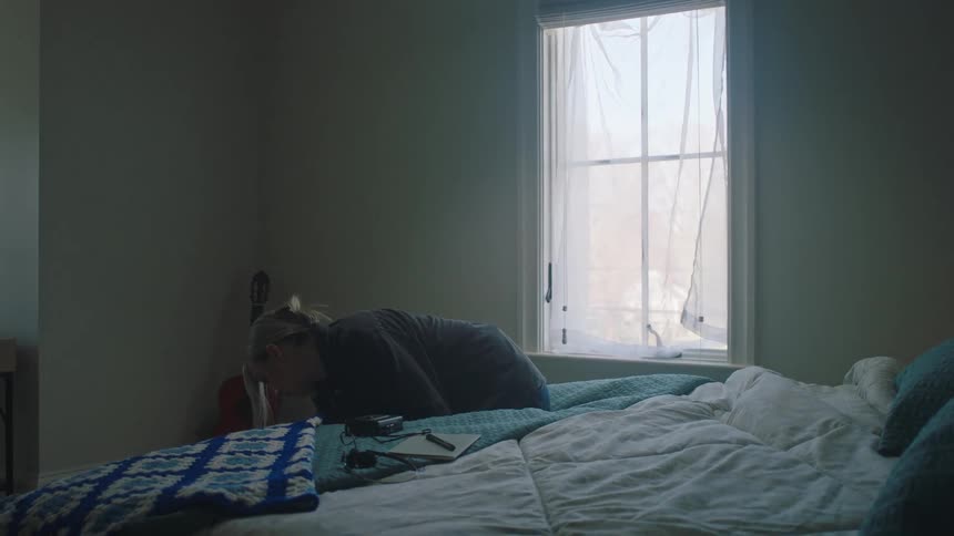 Blonde woman wearing a black shirt and ripped jeans talks on the smartphone in her bedroom