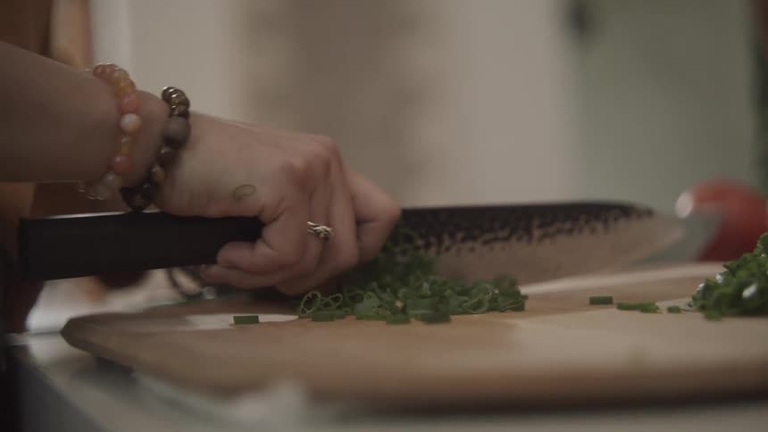 A human hand is cutting green vegetables using a large sharp knife