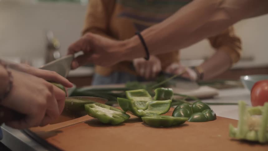 Three people cutting and preparing vegetables for cooking including bell peppers