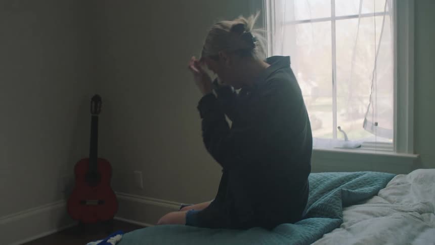 Lady walks around in a room while making a call then sits on the bed afterwards