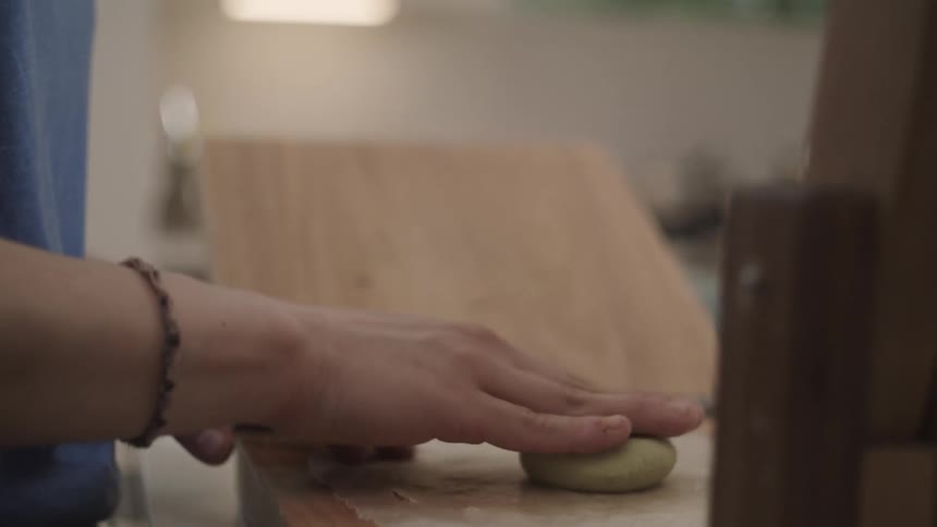 A person presses a small mound of dough atop a wooden cutting board