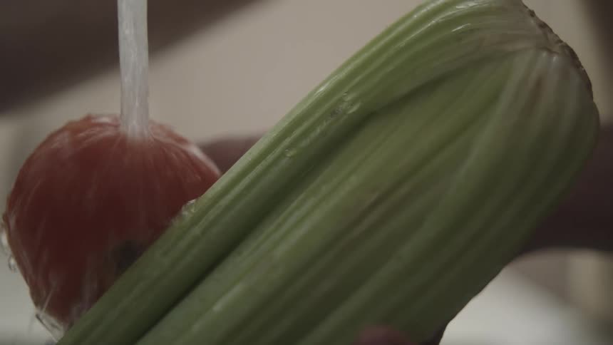 Water from a tap cleaning a tomato that is next to a chayote