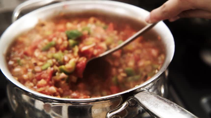 Cook stirs stew boiling in pot on stove