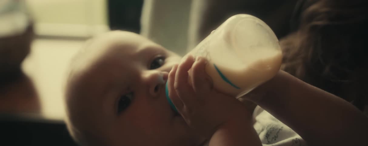 A baby is drinking a bottle in his mothers arms