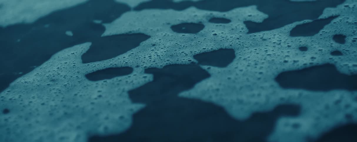 A think layer of foamy bubbles on the surface of water begin to pop