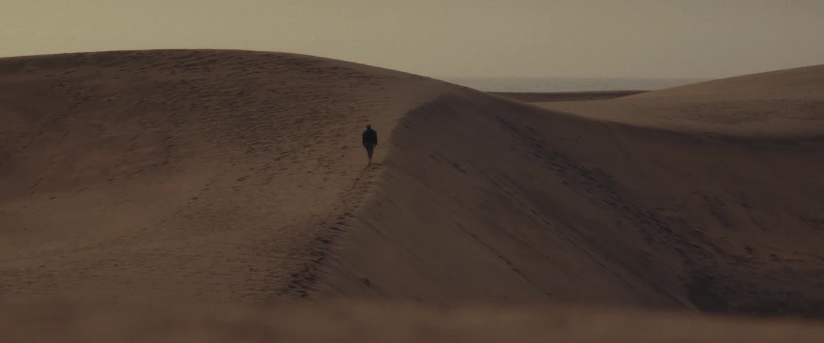 A person walking over sand dunes in the desert