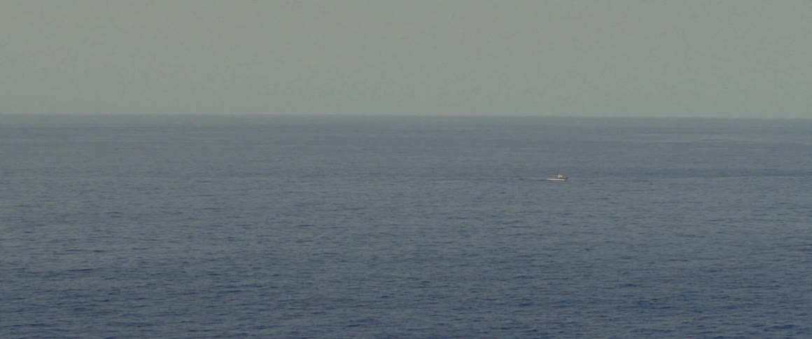 A boat sails across open water as it ripples and waves under a hazy sky