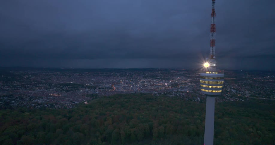 Aerial panoramic of a german city beside the forest and stuttgart telecommunications tower at night with a deep blue sky in the background