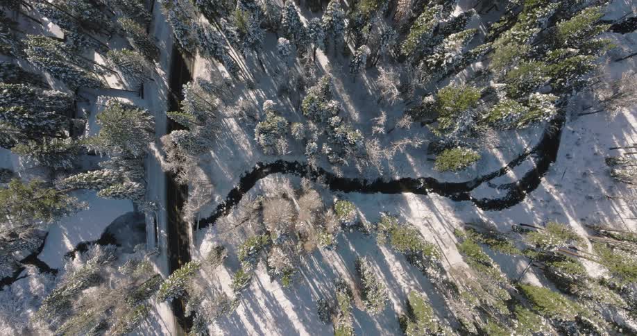 Aerial view looking down on a road through a snowcovered forest with a narrow river