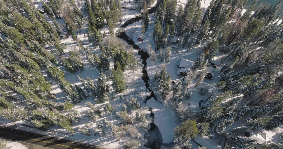 Aerial view along a river in the middle of a snow covered forest that empties into a blue lake on a sunny day