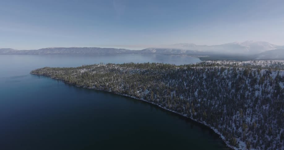 Aerial panorama of a mountain range with conifers covered in snow next to the sea