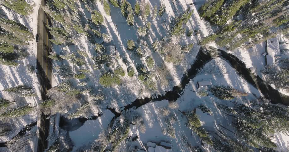 A region with trees and snowy ground next to a road and next to it there is a river