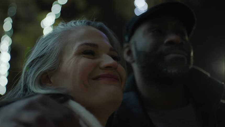 Older man hugs older woman as the couple stands outdoors near a decorated tree