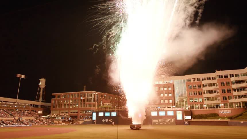 A group of people are watching fireworks on the baseball field