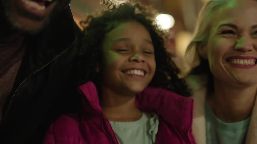 Family smiles and laughs while watching near brightly lit building at night