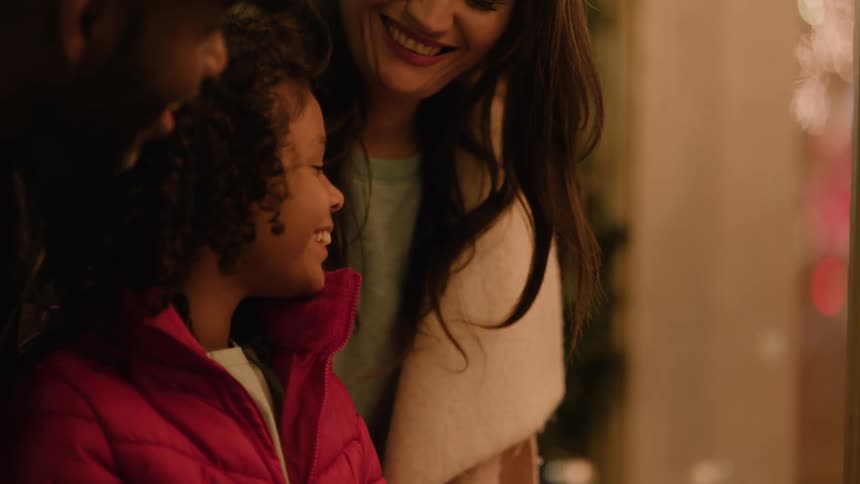Man woman and a child talking smiling while standing outside a shop window at night