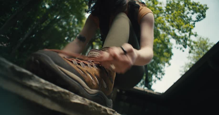 Lady ties her shoe lace near a tree at midday