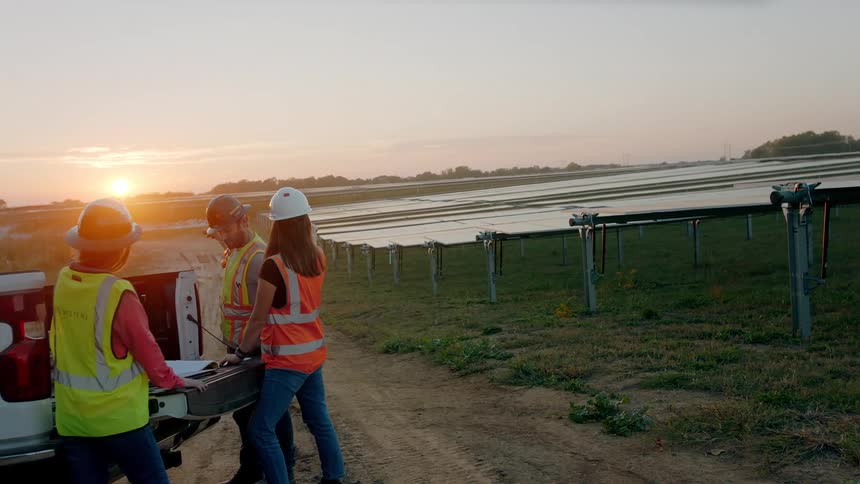 Workers in safety clothing next to a car with the sunset on the horizon