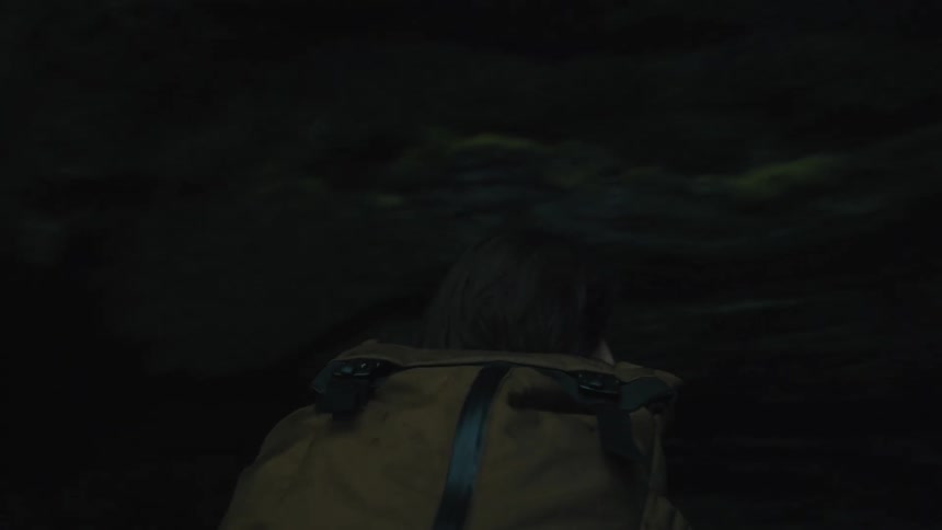 A woman reaches her arm out of the cave to touch the waterfall