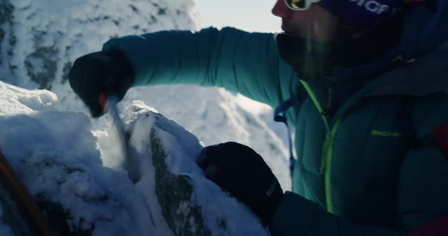 Man climbing a snowcovered mountain and clearing the rock with a tool