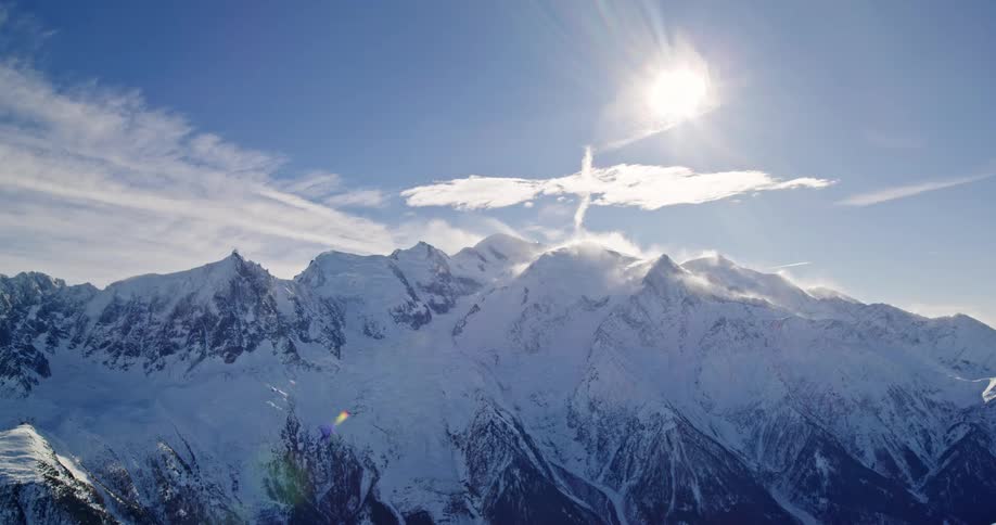 Aerial view of the sun shining over snowy mountains from above