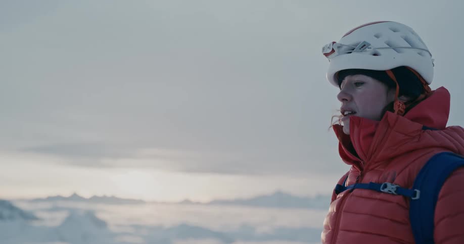 Closeup of a woman adjusting her protective helmet amidst the mountains with a morning sky