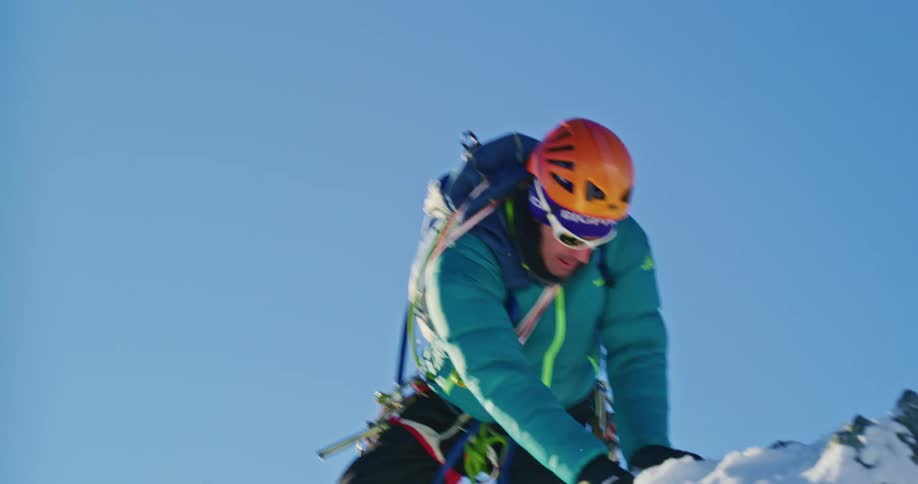 Man reaches the top of a snowy mountain while snow mountaineering