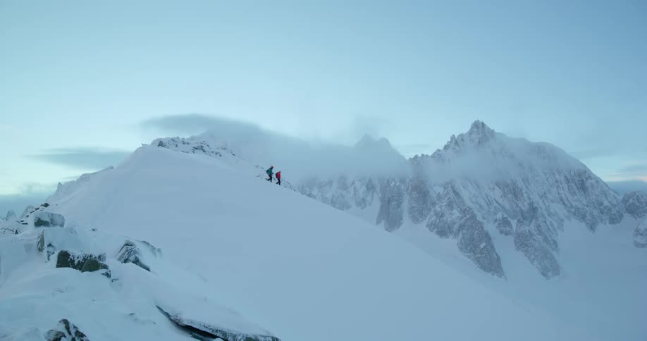 Hikers walk along a snow covered mountain ridge at dusk