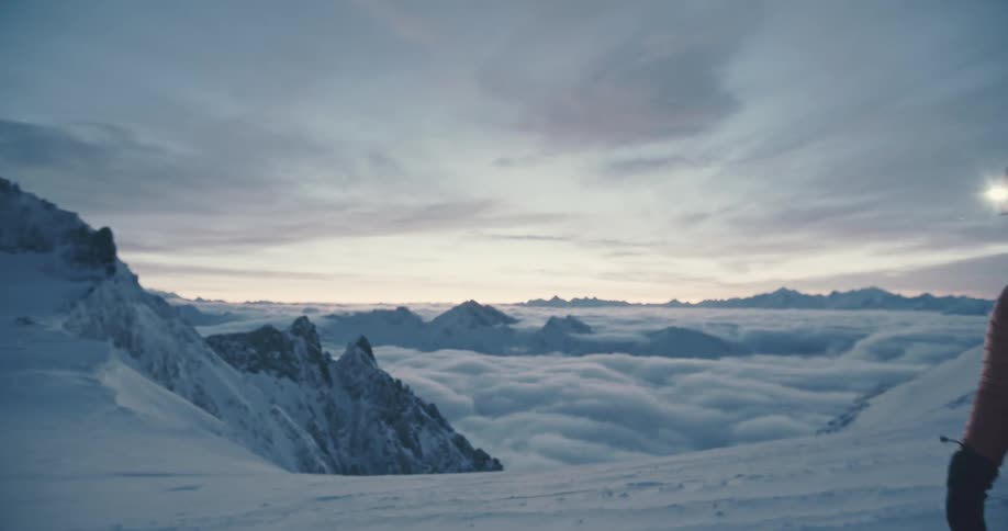 A man is walking on top of a snowy mountain above the clouds
