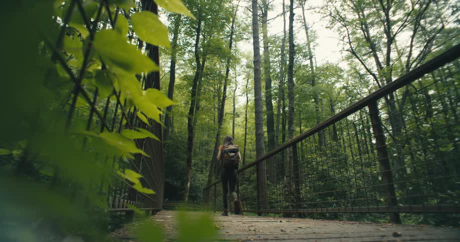 Young woman hikes on a bridge through the forest