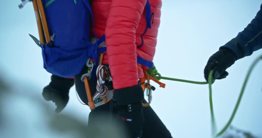 Male climber standing on mountain coils rope attached to female climber