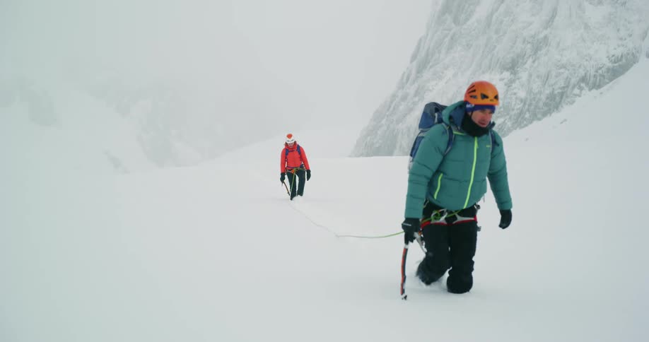 Hikers dressed for extreme weather roped together trekking through high snow up a mountain covered in a snowy white haze