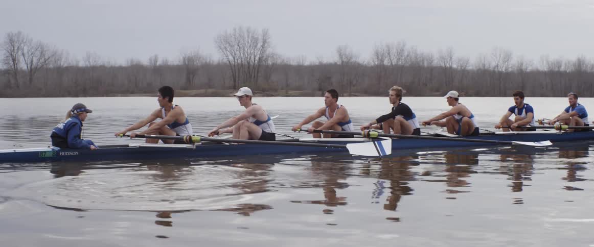 A rowing crew rows a boat across the water