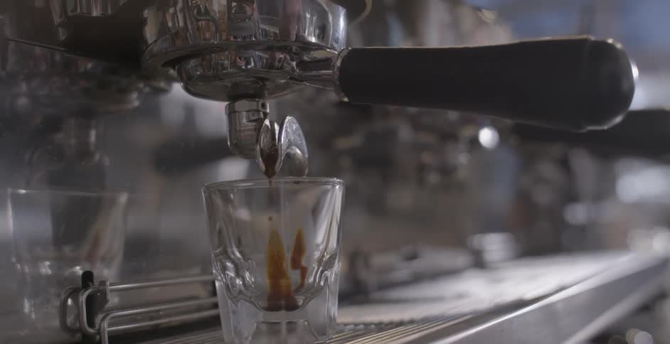 A glass placed beneath an espresso dispenser is filling up