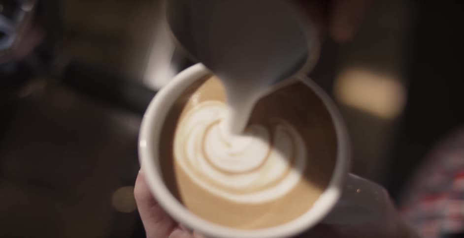 A barista pours creamer in a coffee mug making a leaf shape