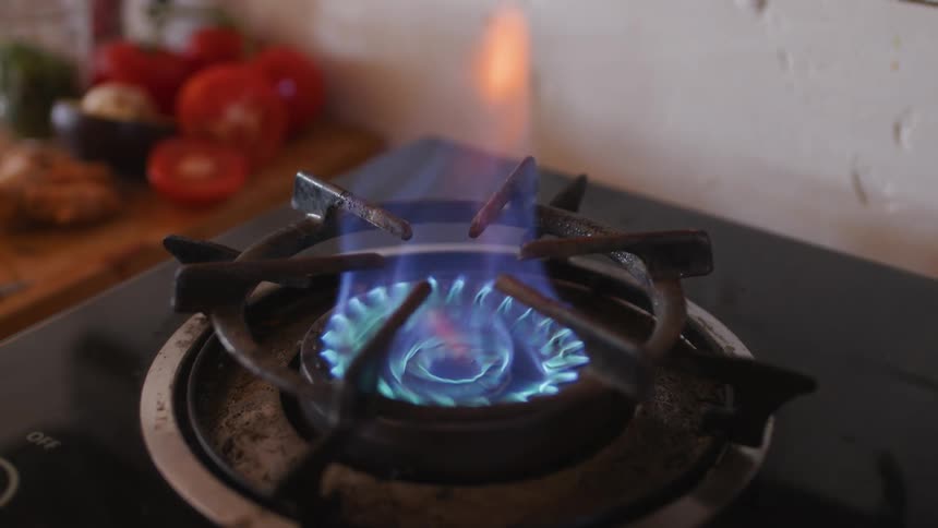 The gas flame on a stove burner turns on and off as tomatoes sit on the counter