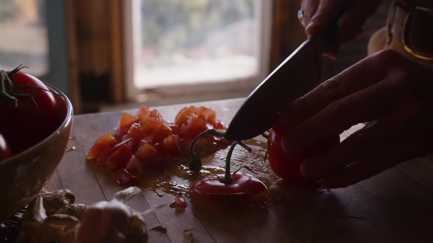 Close up of persons hand cutting up tomatoes with a knife