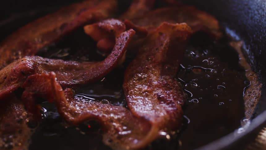 Strips of bacon are frying in a pan