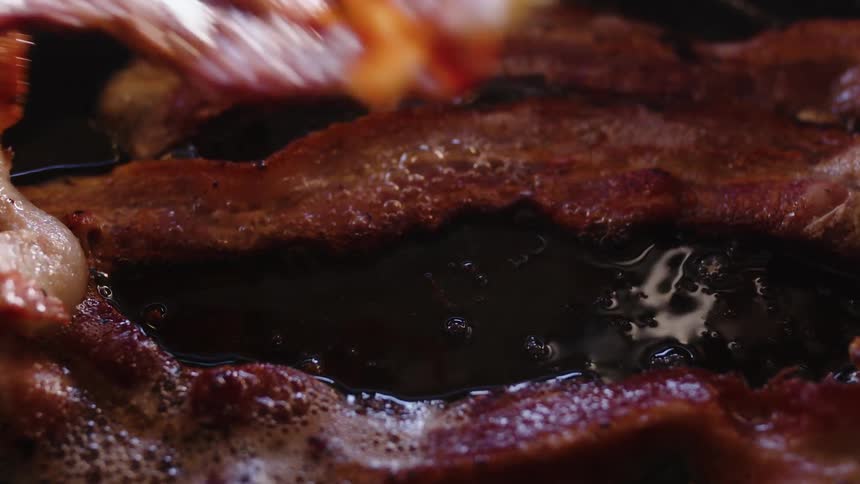 The bacon is being flipped as it cooks
