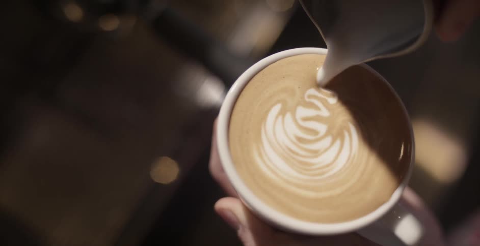 A barista pours creamer in a coffee mug making a leaf shape