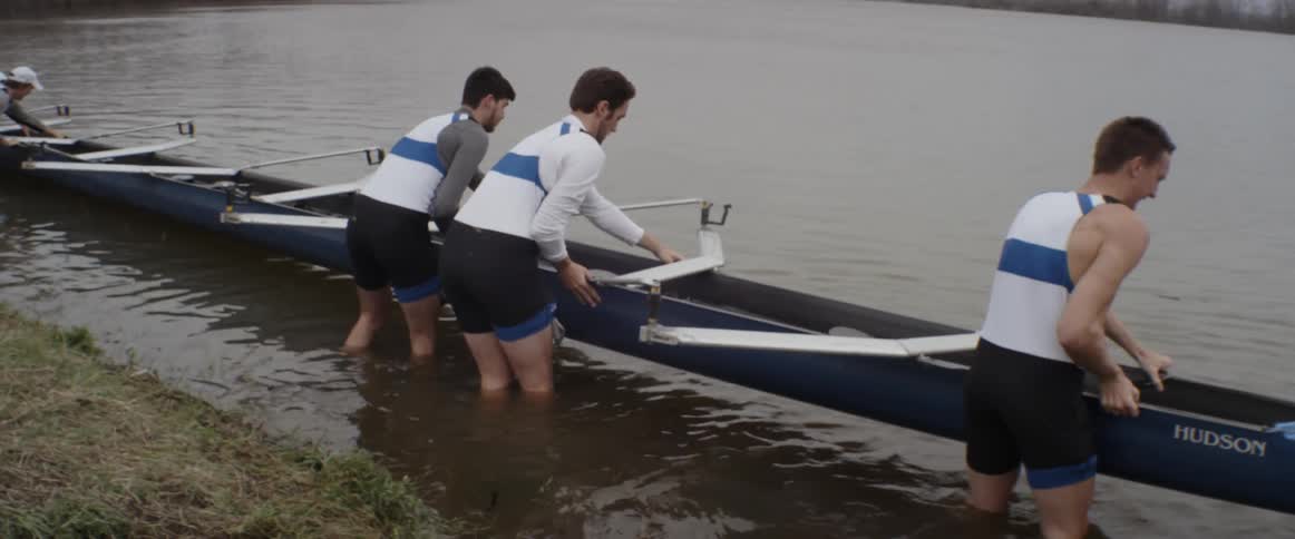 A team of men are placing a rowing scull into the water
