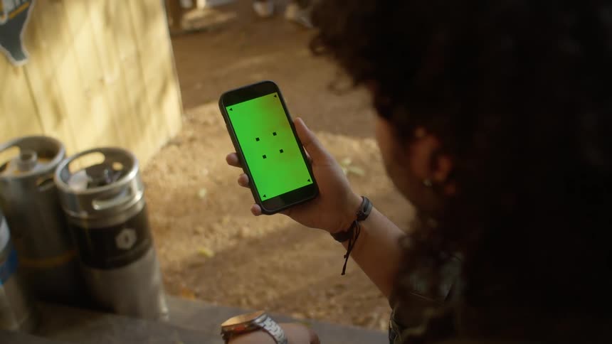 A man is sitting outside holding his cell phone with a green screen