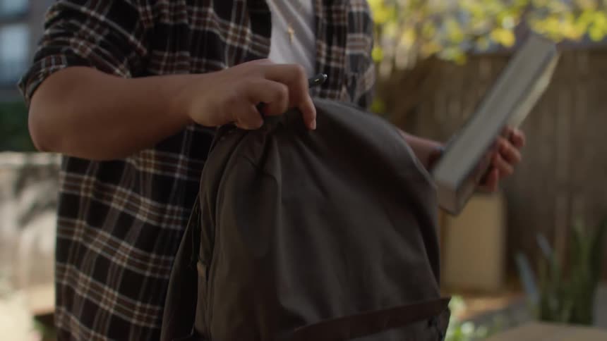 Young man writing and then putting his belongings into his backpack