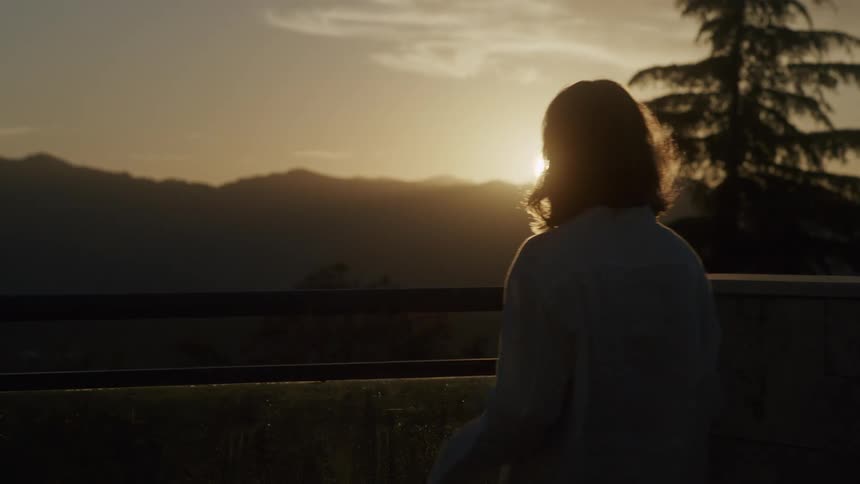 Silhouette of a woman standing on a balcony at sunset